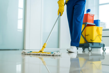 This image showcases a professional cleaning service worker in action mopping the floor in a modern office building The worker is using a mop to clean the floor and a cleaning cart with cleaning supplies can be seen in the background The scene highlights hygiene standards and cleanliness efforts creating a healthy and welcoming environment and portraying professional image for clients and employees in the workspace It emphasizes the importance of maintaining a clean and wellmaintained space for productivity and wellbeingの素材