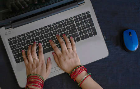 Female wearing bangles and typing on laptop.