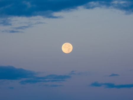 Full moon against brightening dawn sky and blue cloudsの写真素材
