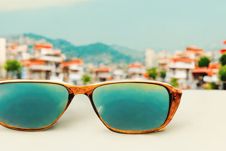 Sunglasses on a white table against the background of a southern seaside city on a sunny day. AI-generated image, not based on any actual sceneの素材