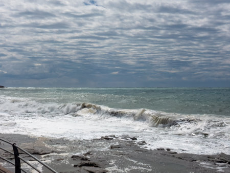 The powerful force of the Mediterranean Sea in stormy cloudy weather as waves crash against a rocky beach. The sky above is filled with atmospheric cloudsの写真素材