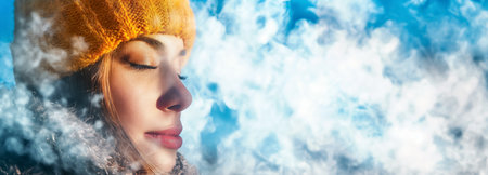 A woman in winter attire exhales visibly cold breath, captured against a vibrant backdrop of a clear blue winter sky.の素材