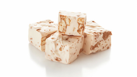 An arrangement of creamy nougat cubes with pieces of almonds, presented on a pristine white surface.の素材