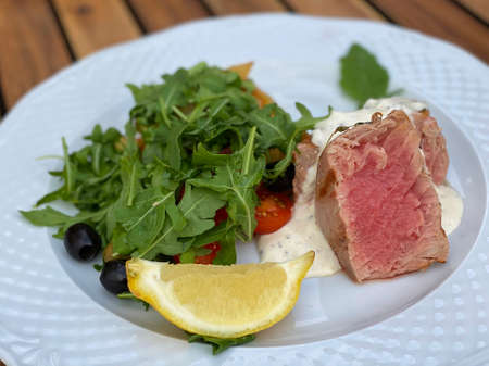 Appetizing grilled tuna dishes poured with sauce with arugula, cherry tomato and olive salad and a slice of lemon.の写真素材