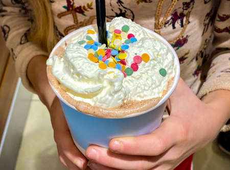 Cocoa with whipped cream decorated with confectionery sprinkles in the hands of a childの写真素材