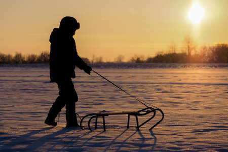 Child with sledge on snow during sunsetの写真素材
