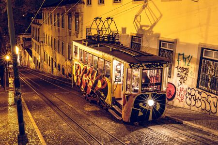 Stop of a cable car in the capital of Portugal. Stop illuminated with lighting at Lisbon and the railroad tracks. The tracks run in the street side buildingの写真素材