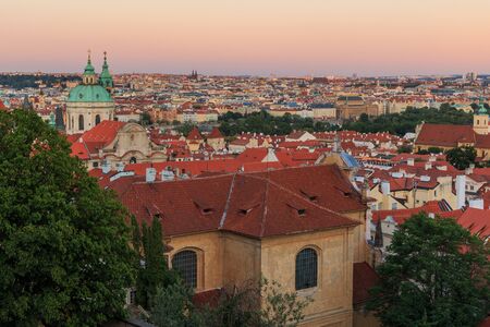 Cityscape over the roofs of the Old Town Prague View from the district Lesser Town with stairs from the Prague Castle with alley, historical buildings and trees in the eveningの写真素材