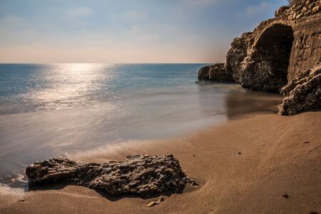 Beach on the Mediterranean coast in Nerja. Sandy beach on the Spanish coast of Costa del Sol. Stone in the sandy beach with rocks and stone arch on sunny day with blue sky and cloudsの写真素材