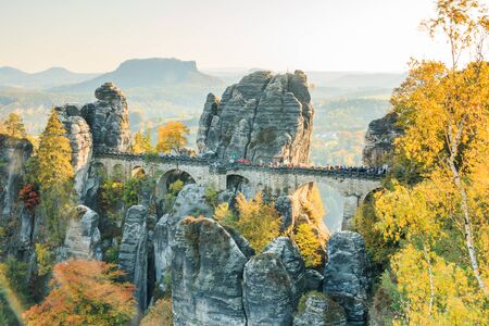 Historic Bastei bridge in Saxon Switzerland in autumn. Rocks and trees with blue sky and sunshine. Elbe valley with mountains in the backgroundの写真素材