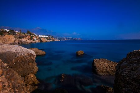 Beach section on the Spanish coast of Costa del Sol in Nerja. Sunny day with blue Mediterranean waters with rocks and city in the backgroundの写真素材