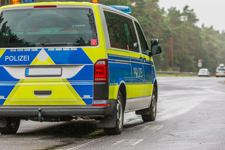 Police car on the Autobahn in the state of Brandenburg. Asphalted road surface in rainy weather. Angled view of the vehicle from behind. yellow and blue paintwork. Trees and guard railsの写真素材
