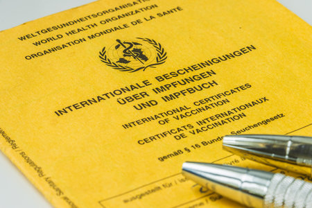 World Health Organization yellow vaccination book and two ballpoint pens. Cover sheet of the yellow vaccination certificate with proof of vaccinations. Travel document in three languagesの写真素材