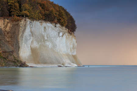 Chalk cliffs on the island of RÃ¼gen in the Jasmund National Park. The water has a smooth surface, shimmering turquoise and in the background is orangeの写真素材
