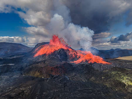 Aerial view of the crater opening from Fagradalsfjall volcano. Crater with strong lava flow on Iceland in the GeoPark. Daytime volcanic eruption on Reykjanes peninsula. Clouds and steam in the skyの写真素材