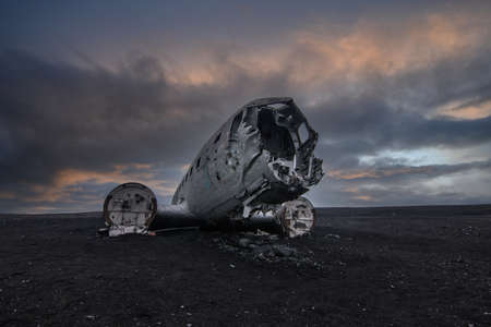 Old plane wreck on black sand in Iceland. Silver colored old airplane without engines on the ground in the evening with dramatic clouds at sunset. Abandoned place on Icelandの写真素材