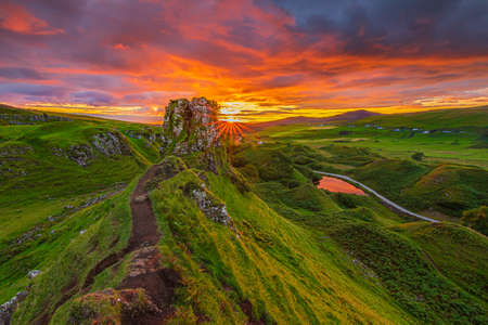 Landscape in Scotland on the Isle of Skye in the evening. Summer sunset with Castle Ewen rock. sun star on the horizon. path on the cliff edge. Road with a small lakeの写真素材