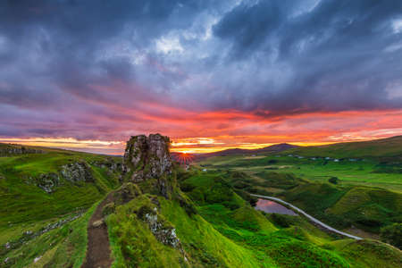 Landscape of an evening mood with sunset in Scotland. Isle of Skye in Scotland in summer. Sun star on the horizon next to Castle Ewen rock. Colorful clouds in the sky. Green meadows and hillsの写真素材