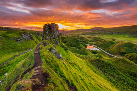 Sunset on the Isle of Skye in Summer. Landscape with rocks Castle Ewen. Sandy road to rocks and hills with green grass. Colorful sky with clouds. Road and small lake in the backgroundの写真素材