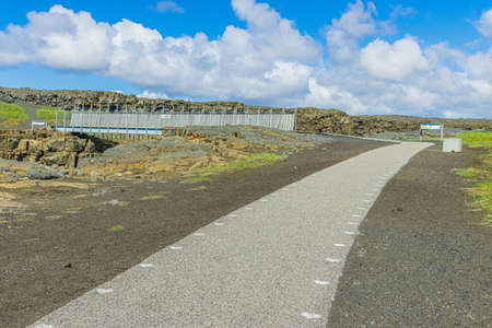 Landscape with a path to a metal bridge on Iceland of the Reykjanes peninsula. Lava rocks across the North American and Eurasian fissures. brown and gray lava rock with black sandの写真素材