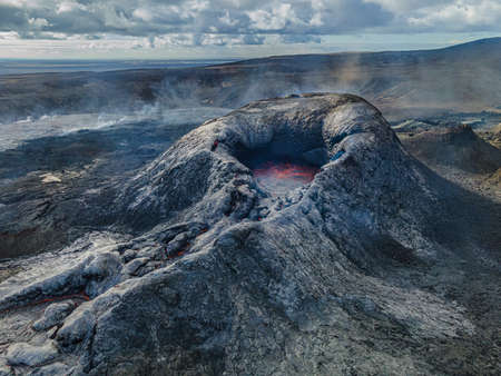 Landscape in Iceland. Volcanic crater on Reykjanes Peninsula by day. Crater before eruption. Dark cooled lava around the crater and steam. Dark rock and clouds in the skyの写真素材