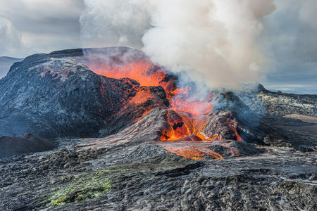 Heavy steam and smoke over a volcanic crater. Glowing red lava flows from an active crater....