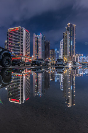 Reflections from skyscrapers and parked cars in Dubai at night time. City of United Arab Emirates at blue hour. Illuminated financial center skyline with evening cloudsの写真素材
