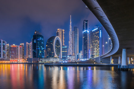Dubai at night. City skyline in United Arab Emirates. Skyscrapers illuminated at the blue hour with a curved course of a bridge. Reflections on the water surface in the portの写真素材