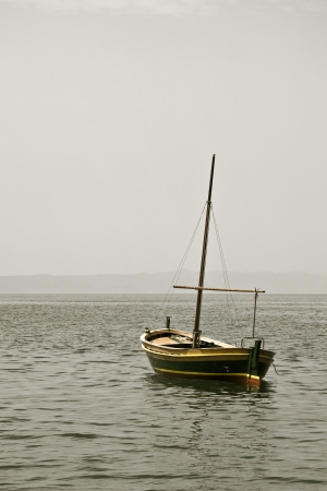 Small wooden fishing boat with a mast in water の写真素材