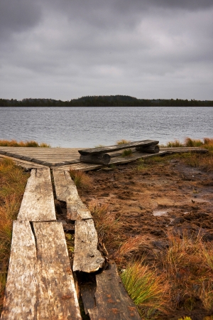 Wooden road lead to a resting place with a bench and large lake in a marshの写真素材