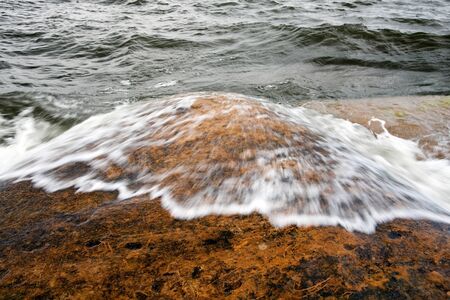 sea waves going over a brown-orange rock in the seaの写真素材