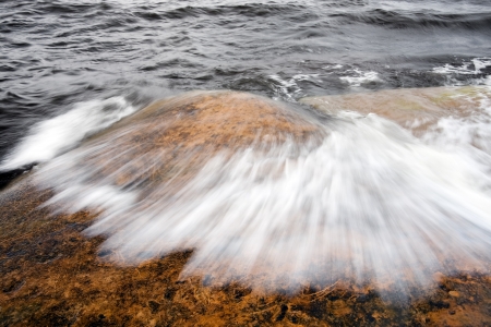 sea waves going over a brown-orange rock in the seaの写真素材