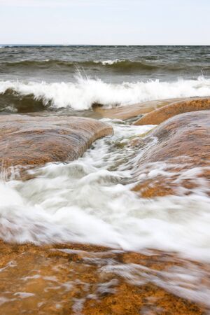 sea waves foaming on the large orange rocksの写真素材