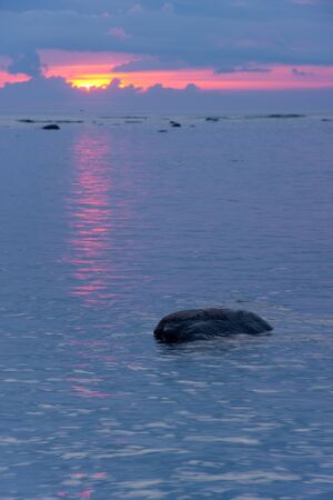 One stone in blueish sea at sunset  Sunlight reflects on seaの写真素材