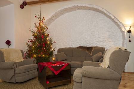 Living room furnished with big and soft couch and armchairs and a decorated illuminated shiny natural christmas tree   fir-tree in the left cornerの写真素材