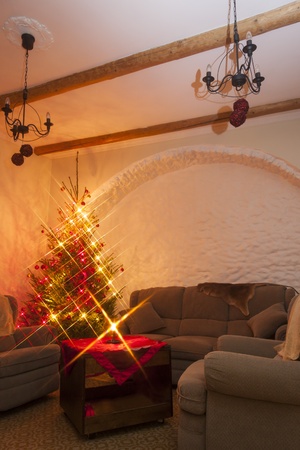 Dark living room furnished with big and soft couch and armchairs and a decorated natural christmas tree   fir-tree in the left cornerの写真素材