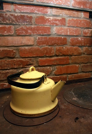 Yellow tea pot on a stove, red brick wall in backgroundの写真素材