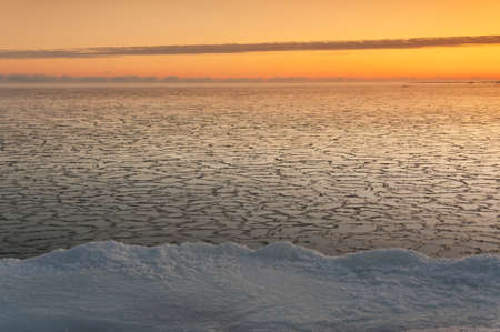 Icy sea at sunrise, snowy land in foregroundの写真素材