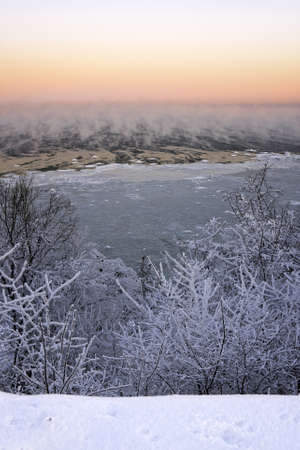 Steaming and icy sea and snowy forest  at cold winter morningの写真素材