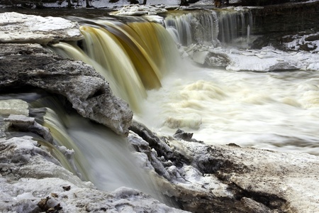Flowing waterfall called Keila Juga in Estonia with large piece of ice and melting snow at winter の写真素材