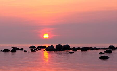 Black rocks in sea at sunset  Sun still in the sky の写真素材