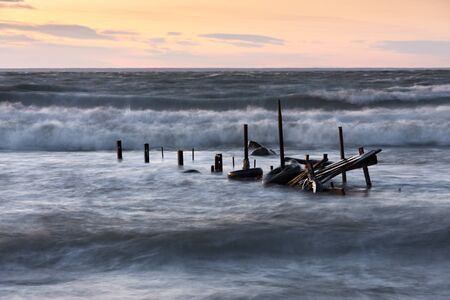 Broken timber foot bridge in sea and partly under water due to high tide at sunsetの写真素材