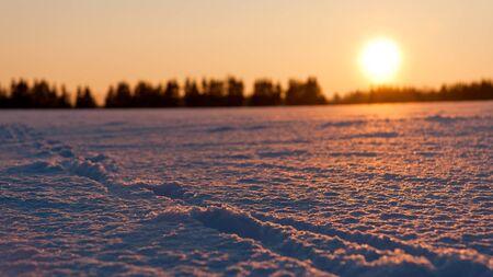 Golden sunset behind snow field with foot prints or tracksの写真素材