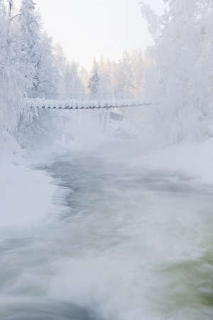 Bridge obove vaporing river in snowy forest in Finlandの写真素材