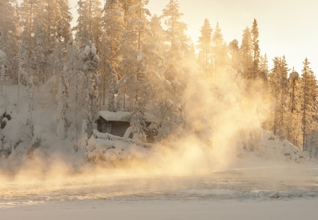 Small log cabin behind vaporing river in winter in Lapland, Finlandの写真素材