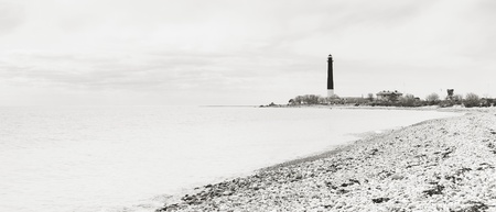 Tall slim black beacon or lighthouse in distance near seaの写真素材