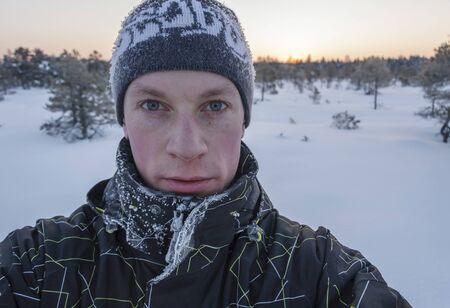 Portrait of a young man with frosty clothes and hat in a marsh early in the winter morning