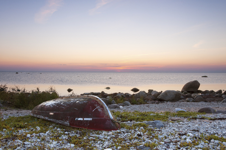 Red fishing boat upside down at coast at sunsetの写真素材