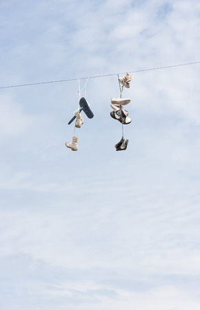 Many old worn boots or shoes hang on an electric cableの写真素材
