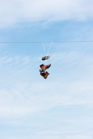 Many old worn boots or shoes hang on an electric cableの写真素材
